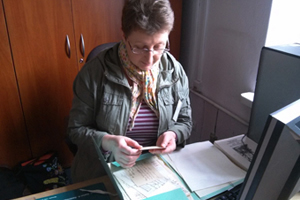 Zdjęcie, na którym widać osobę pracującą przy opisywaniu archiwaliów - rękopisów prac naukowych i notatek wielkich archeologów.