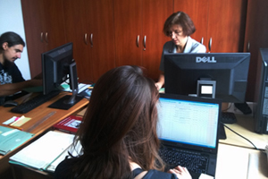 Zdjęcie, na którym widać trzy osoby pracującą przy opisywaniu archiwaliów - rękopisów prac naukowych i notatek wielkich archeologów.